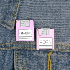 Nahaufnahme der rosa Disketten-Emaille-Pins mit Vaporwave-Text auf blauem Denim-Stoff