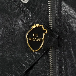 Macro d'une broche en émail cœur anatomique avec texte Be Brave sur veste en cuir