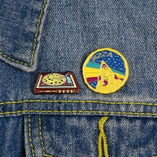 Detailed view of pizza and turntable enamel pins pinned on blue denim fabric
