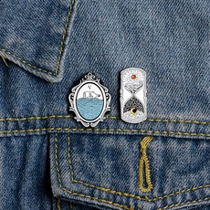 Detail view of retro hourglass and message bottle enamel pins on a denim jacket pocket
