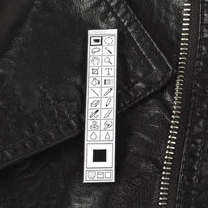 Nahaufnahme einer Metall-Emaille-Brosche mit Photoshop-Symbolleisten-Icons auf schwarzem Leder