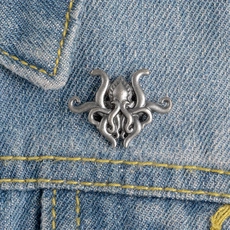 Detail of silver Cthulhu octopus metal brooch pinned on blue denim jacket fabric