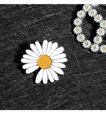 Macro detail of enamel daisy brooch with white petals and yellow core on black background