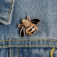 Detailaufnahme einer goldfarbenen Bienen-Emaille-Brosche auf blauem Denim-Stoffgewebe