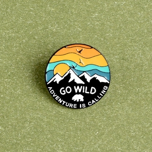 Enamel pin detail showing sunset snow mountain and eagle with GO WILD slogan text