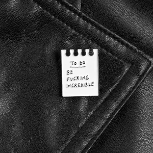 Notebook enamel pin with TO DO BE FUCKING INCREDIBLE text on black leather jacket