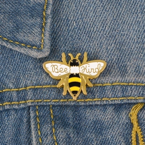 Close-up of a Bee Kind enamel pin with gold plating on a blue denim jacket texture
