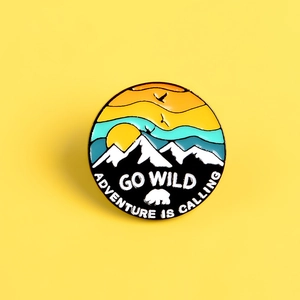 Detail of enamel pin with sunset mountain, bear and Go Wild adventure text
