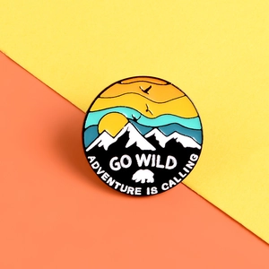 Detail of enameled mountain brooch with GO WILD and ADVENTURE IS CALLING text on orange background