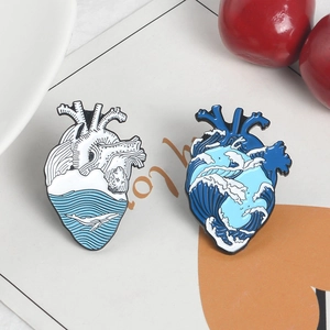 Set of two heart shaped enamel pins featuring creative blue wave and whale ocean motifs