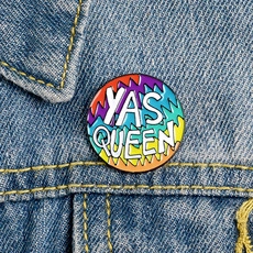 Close-up of a rainbow YAS QUEEN badge pinned on blue denim fabric texture