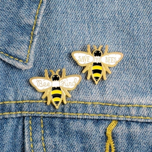 Détail de broches abeille en émail avec slogans Save the Bees et Bee Kind sur denim