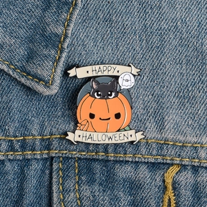 Close-up of Halloween enamel pin with orange pumpkin and black cat on denim jacket