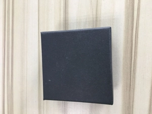 Bovenaanzicht van een vierkant zwart sieradendoosje met matte textuur op houtbasis