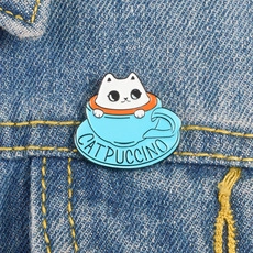 Detailed view of an enamel Catpuccino pin attached to a dark blue denim jacket fabric