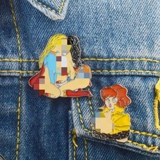 Detail of colorful enamel pins on denim jacket showing superhero cat coffee cup art