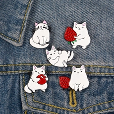 Lot de cinq broches chat blanc en émail avec fraises sur une veste en jean bleue
