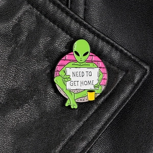 Green alien enamel pin with NEED TO GET HOME slogan on a black leather jacket lapel