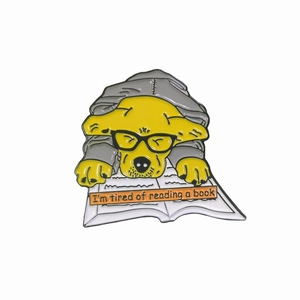 Détail du pin's émaillé chien jaune mignon se reposant sur un livre avec slogan