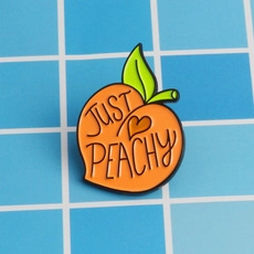 Detail of peach enamel pin with 'Just Peachy' text on blue checkered background