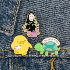 Three cartoon enamel pins including No-Face and turtle on blue denim fabric background