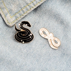 Close-up of snake enamel pins in black and white colors on blue denim fabric