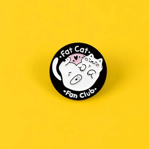 Detail of round black enamel Fat Cat Fan Club pin with cute white cat on yellow background