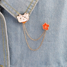 Close-up of cat and red plum flower enamel pins joined by dual gold chains on denim