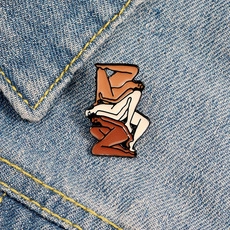 Artistic enamel brooch featuring intertwined figures displayed on blue denim fabric