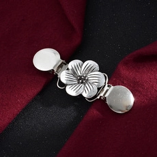 Macro detail of silver floral cardigan clip on dark red fabric showing metal texture
