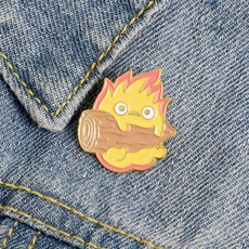 Detailed close-up of Calcifer enamel pin on blue denim with vivid yellow flame details