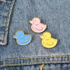 Close-up of cute pink, blue and yellow duck enamel pins on blue denim fabric texture