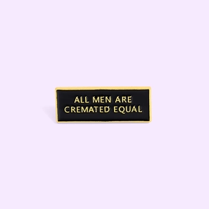 Detail of rectangular enamel brooch with All Men Are Cremated Equal slogan on black background