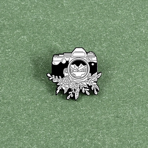 Macro detail of retro camera enamel pin featuring mountain scenery and floral engraving
