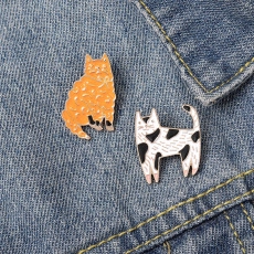 Detailed macro view of cute orange and tuxedo cat enamel pins on blue denim fabric