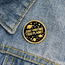 Macro shot of black enamel JUST VISITING THIS PLANET pin badge on blue denim jacket