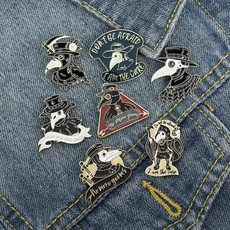 Detail showing seven plague doctor enamel pins arranged on blue denim fabric background