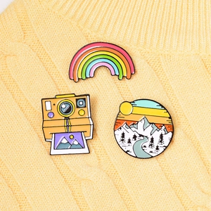 Detailed view of rainbow, camera, and mountain enamel pins on a yellow knit sweater