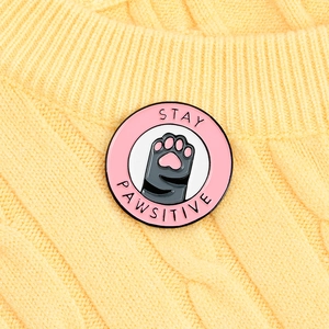 Cute pink cat paw enamel pin with Stay Pawsitive slogan on a yellow knit sweater