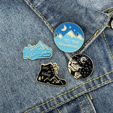 Detail view of 4 enamel outdoor hiking pins featuring mountain and boot designs on denim