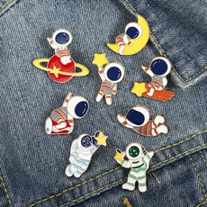 Detailed view of creative astronaut enamel pins displayed on blue denim fabric background