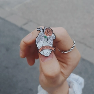 Artistic enamel heart pin with pink rose and banner slogan held in hand