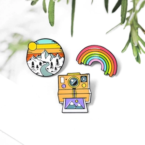 Three-piece enamel pin set with rainbow, vintage camera, and mountain scenery designs