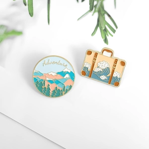Detail of enamel adventure mountain and wave luggage pins on a minimalist background