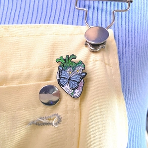 Detail of anatomical heart enamel pin with daisy and butterfly on canvas overalls