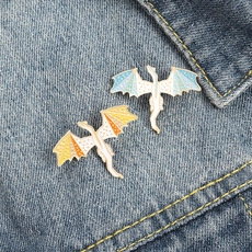 Detail of two dragon enamel pins in blue and yellow attached to denim fabric texture
