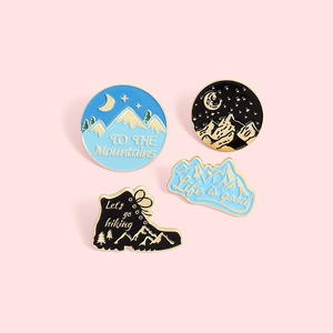 Detailed view of four outdoor hiking enamel pins featuring snow mountains and hiking boots