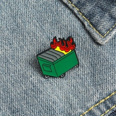 Detailed view of a green enamel dumpster fire pin featuring red flames on denim fabric