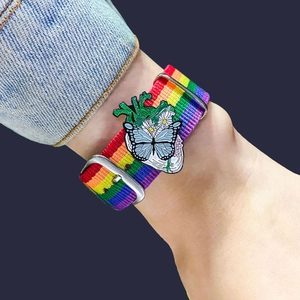 Close-up of rainbow fabric watch strap with a detailed butterfly and heart enamel charm
