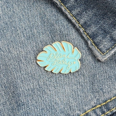 Detail of a Plant Lady enamel pin with light blue leaf design on blue denim jacket